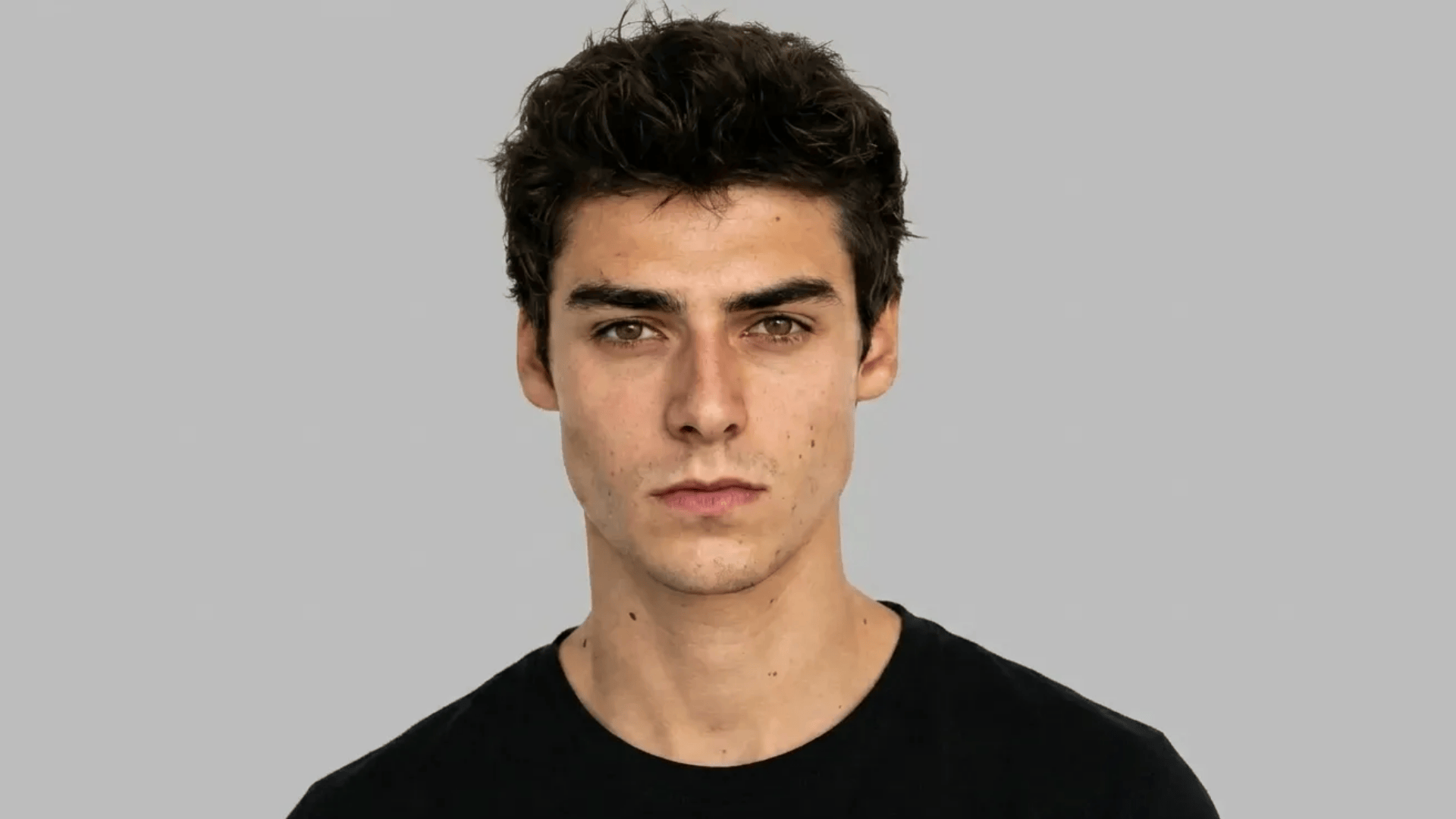 Close-up of a person with thick, textured hair, balanced facial features, and a defined jawline against a plain background.