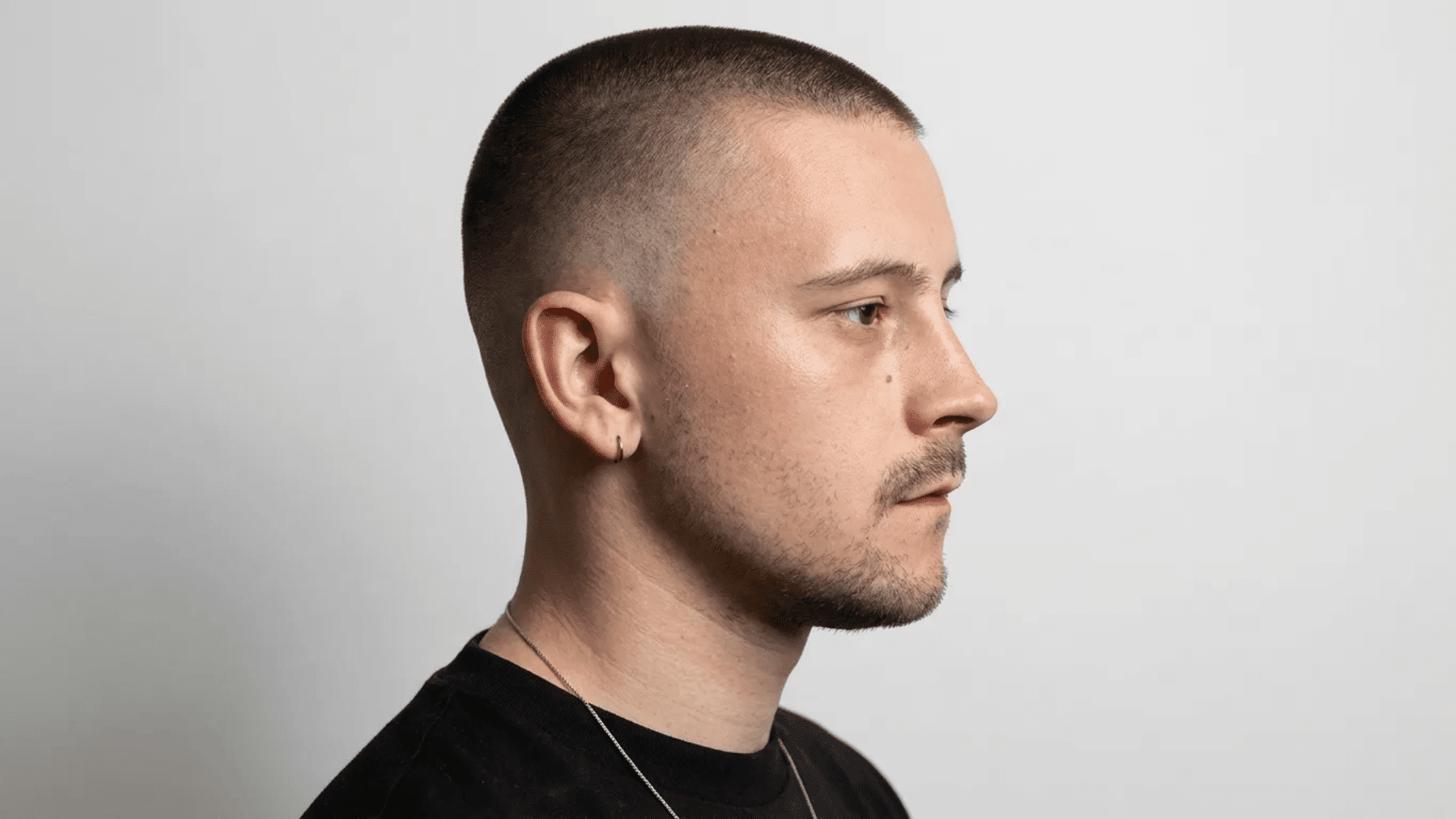 Side profile of a person with a clean buzz cut, showing even hair length, defined jawline, and visible scalp outline.